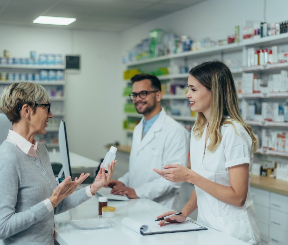 pharmacist-working-on-a-computer-while-female-pharmacist-is-giving-medications-to-senior-patient.jpg